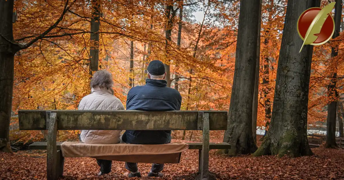 Elderly couple sitting on a bench in autumn forest.