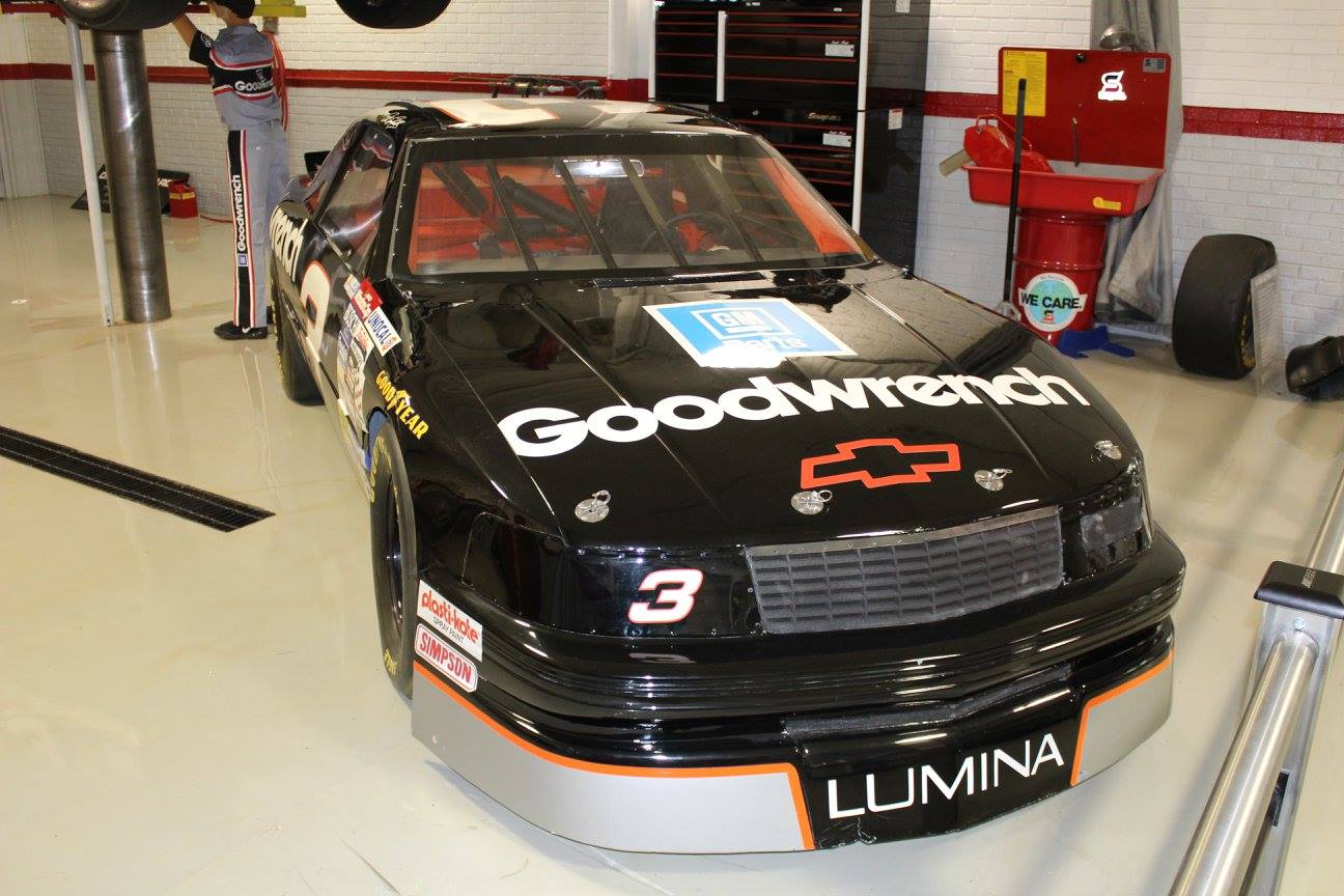 Black NASCAR race car in garage with Goodwrench branding.