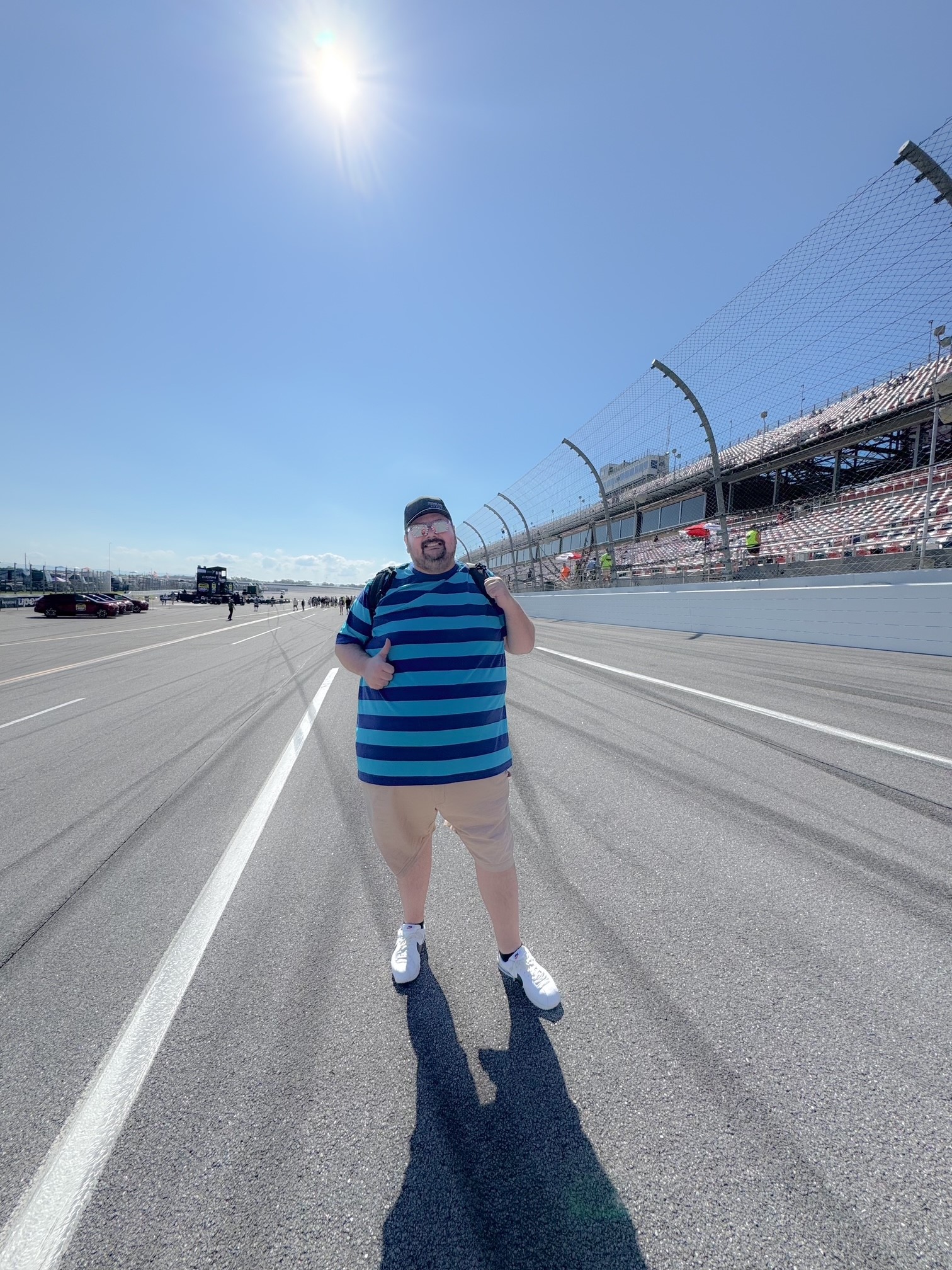 Person standing on sunny racetrack with bleachers