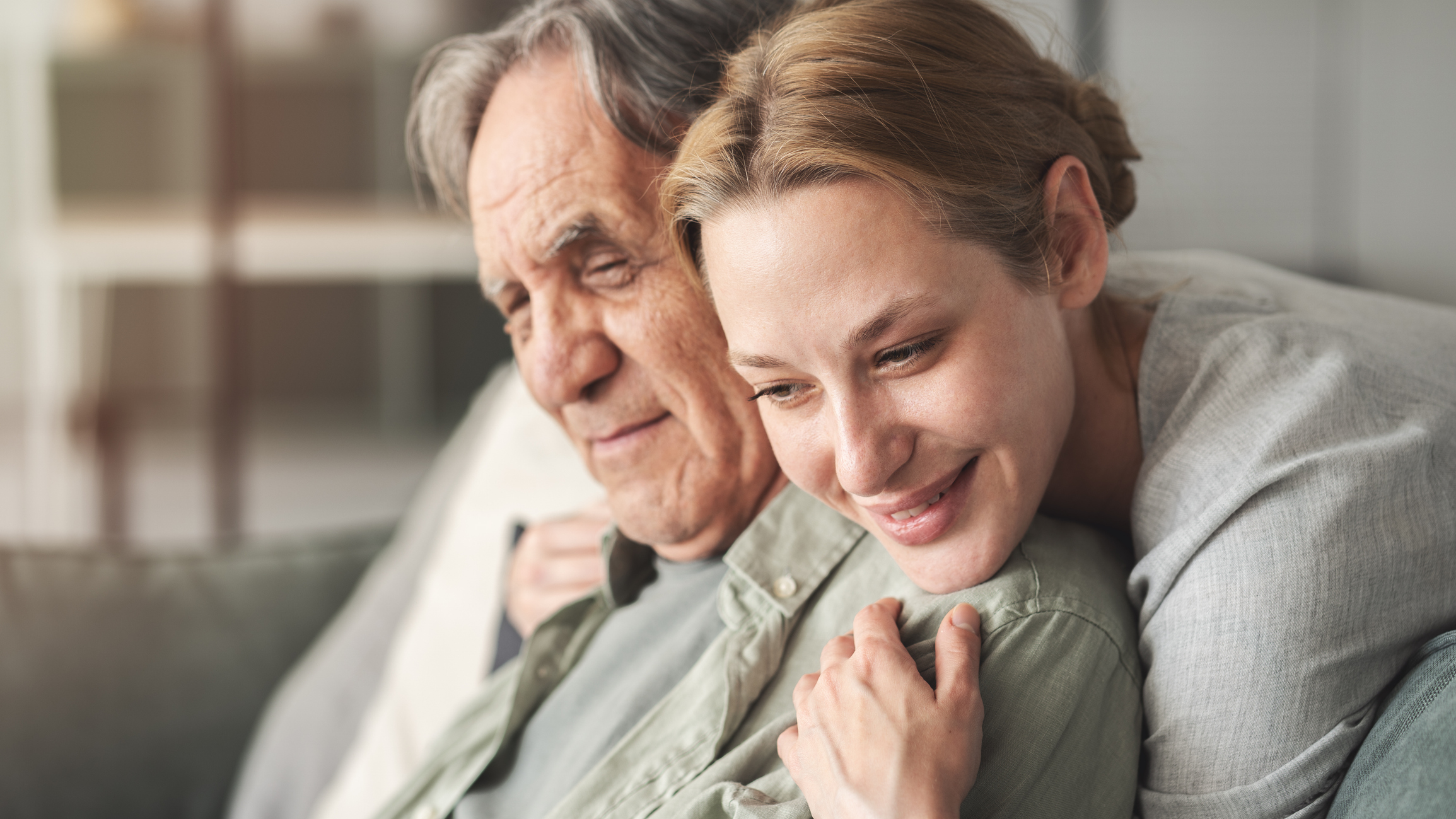 Woman hugging elderly man affectionately on couch