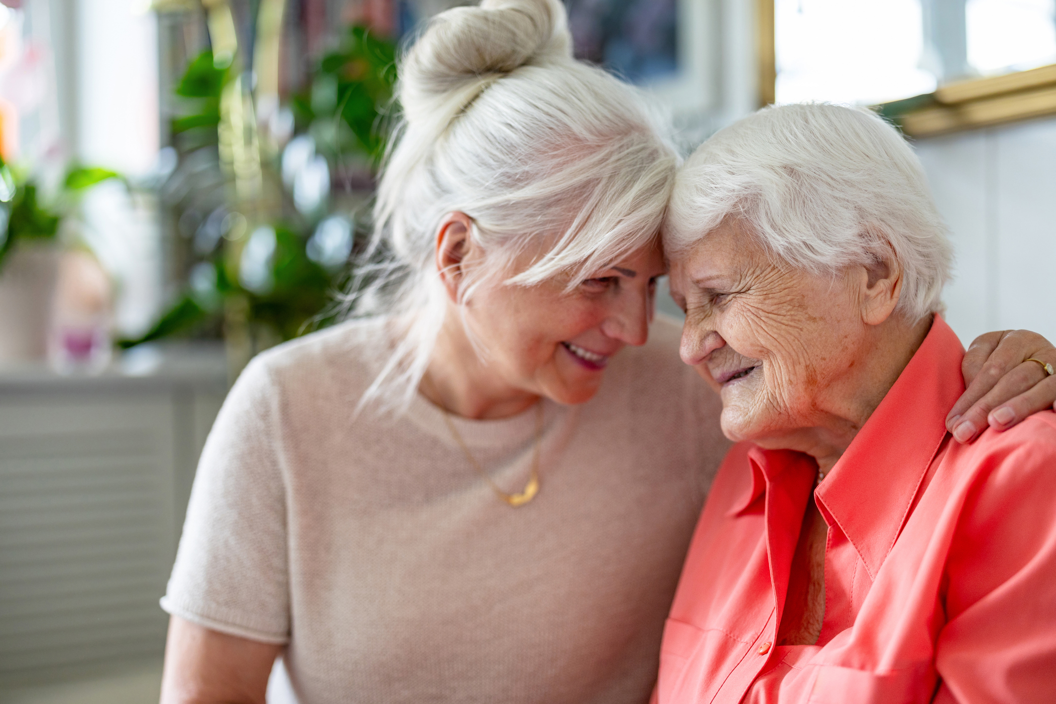 Adult daughter affectionately embraces her elderly mother at home