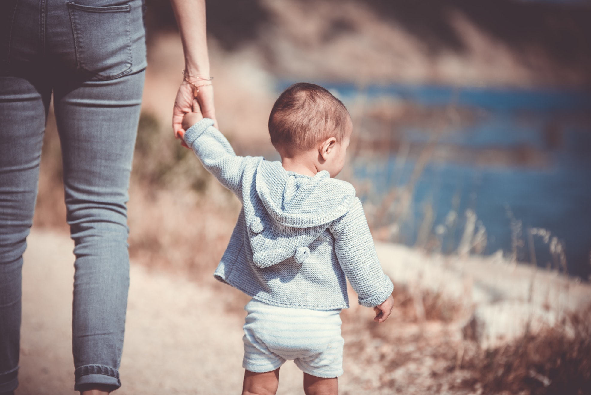 Adult holding toddler's hand beside a lakeside path